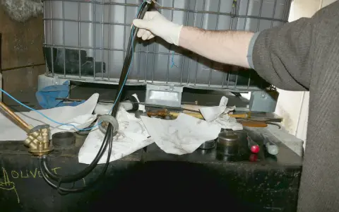 Main d'une personne en gant blanc manipulant un tube avec des fils bleus, près d'une cuve à fioul et d'une crépine.