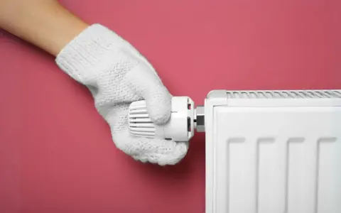 Main tenant, avec un gant blanc, ajuste le thermostat d'un radiateur pour choisir entre le chauffage mode eco ou confort.