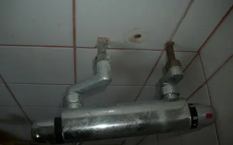 Un excentrique robinet de douche, fixé au mur carrelé, avec des tuyaux argentés et des indications de température.