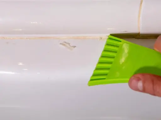 Outil vert raclant du mastic durci sur une surface blanche.