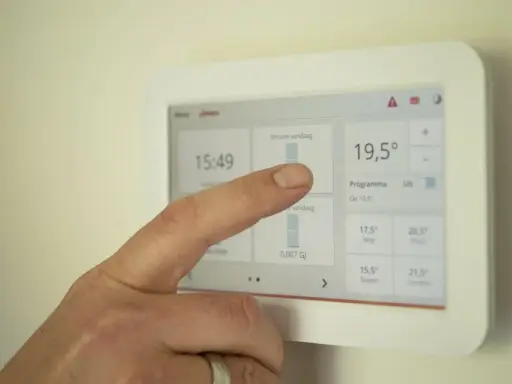 Un doigt interagit avec un écran tactile de domotique affichant la température et les programmes.