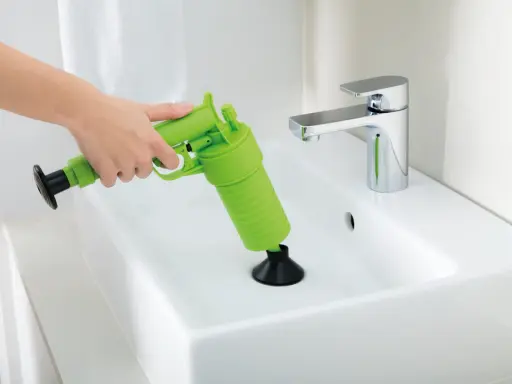 Main verte, un pistolet déboucheur est utilisé pour dégager un lavabo blanc.