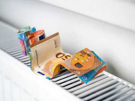Des billets en euros pliés sur un radiateur blanc, symbolisant le coût élevé du chauffage et la **consommation** du **radiateur hors gel**.