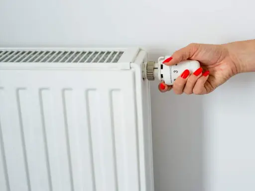 Main d'une femme aux ongles rouges tournant le thermostat pour savoir comment éteindre un radiateur électrique.