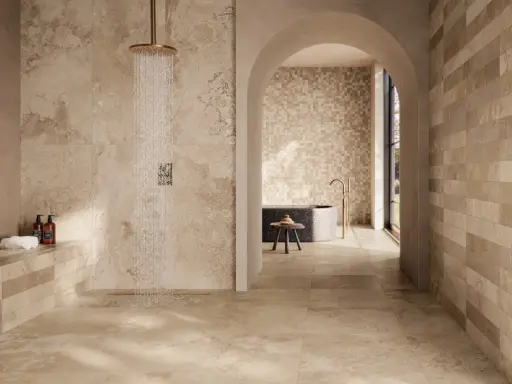 Douche moderne avec robinetterie dorée sur un sol de salle de bain en travertin. L'espace invite à la détente.