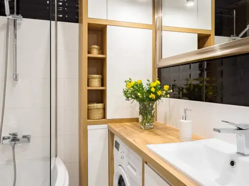Une petite salle de bain moderne avec une douche, un lavabo, une machine à laver et des paniers en osier sur des étagères en bois.