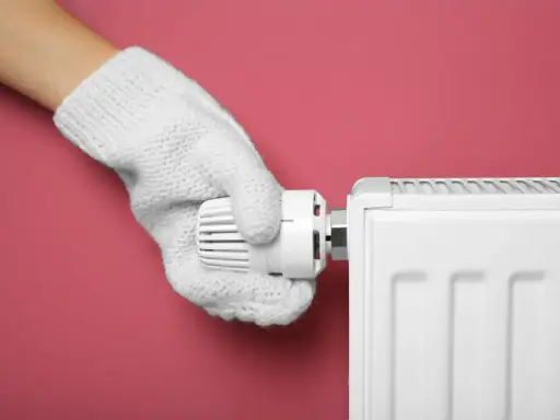Main tenant, avec un gant blanc, ajuste le thermostat d'un radiateur pour choisir entre le chauffage mode eco ou confort.
