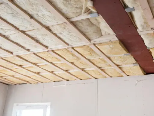 Isolation thermique plafond en cours d'installation, avec des panneaux de laine minérale entre les solives en bois.