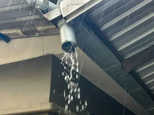 Gouttière en métal sous une pluie battante, l'eau s'écoule abondamment du tuyau, assurant l'évacuation eau de pluie.