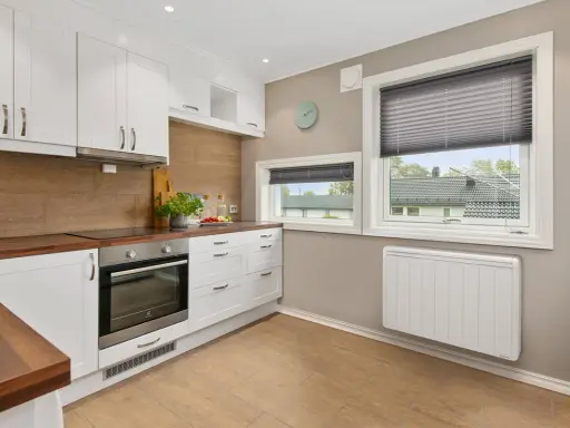 Cuisine moderne avec placards blancs, plan de travail en bois et un radiateur blanc discret assurant le chauffage.