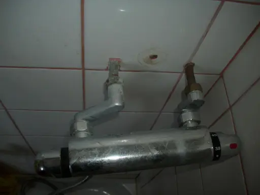 Un excentrique robinet de douche, fixé au mur carrelé, avec des tuyaux argentés et des indications de température.