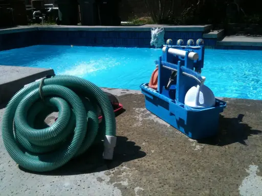 Tuyau vert enroulé et boîte bleue d'accessoires de nettoyage pour le branchement piscine.