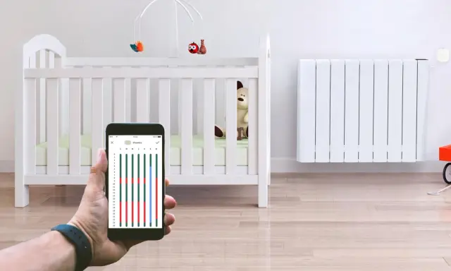 Contrôle du chauffage de la chambre bébé via smartphone. Un radiateur blanc et un lit de bébé sont visibles.