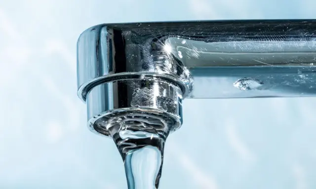 Gouttes d'eau tombant d'un robinet chromé, montrant des dépôts calcaires, un signe du tableau dureté de l'eau.