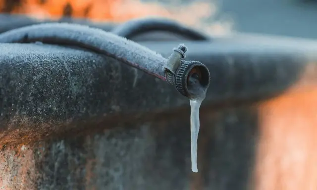 Un tuyau de jardin givré, avec une stalactite de glace tombant du robinet, illustre la nécessité de la protection tuyau en hiver.