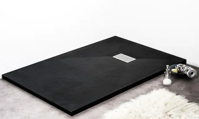 Receveur de douche noir texturé, avec une grille d'évacuation chromée. Un savon et une serviette sont posés sur le bord.