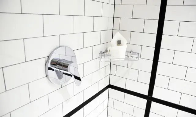 Un robinet de douche chromé et une étagère avec des serviettes sur un mur de carrelage blanc. Idéal pour nettoyer carrelage mural encrassé.