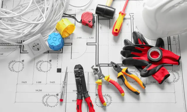 Outils d'électricien et rouleau de câble pour radiateur électrique, prêts pour l'installation sur un plan.