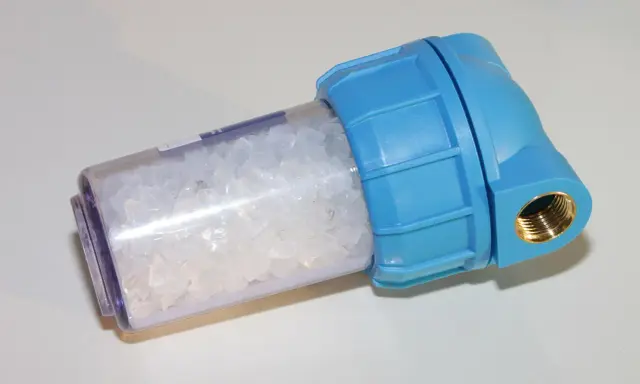 Filtre d'adoucisseur d'eau bleu rempli de cristaux blancs, peut-être une panne à résoudre.