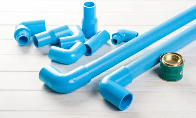 Ensemble de tuyaux et raccords bleus en PVC, prêts pour une installation. Un pot de colle est à proximité.