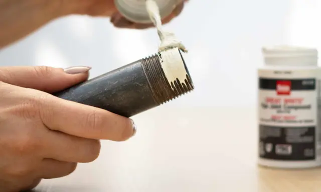 Application de pâte sur le filetage d'un **tube pour joint**. Un pot de pâte est visible à droite.