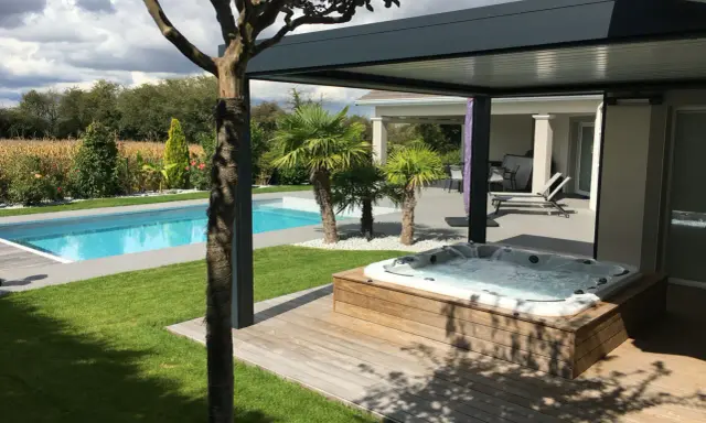 Un spa bouillonnant sur une terrasse en bois, à côté d'une piscine bleue. Le tableau temps de filtration piscine est visible dans le jardin luxuriant.