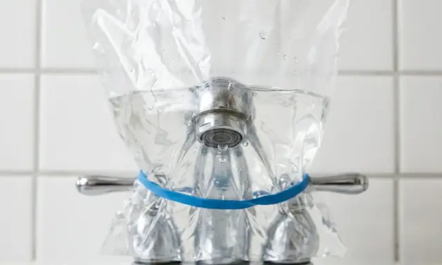 Un sac en plastique rempli d'eau est attaché à un robinet avec un élastique bleu. Une méthode pour enlever le calcaire de l'eau naturellement.