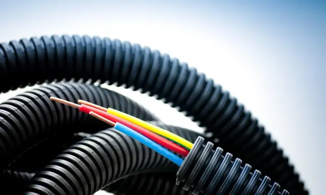 Trois fils électriques colorés sortent d'un tube plastique souple noir et ondulé, prêt à protéger les câbles.
