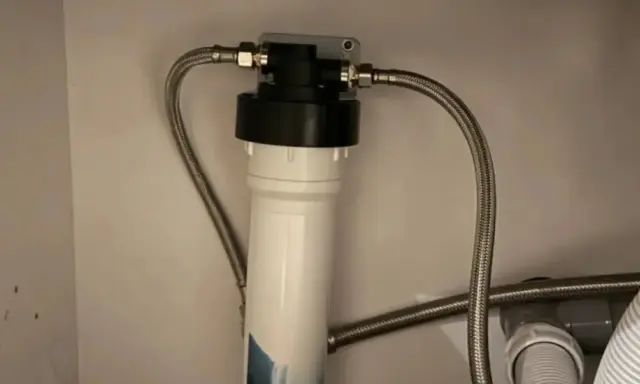 Système de filtration d'eau sous évier avec un cartouche charbon actif blanc et noir, relié par des tuyaux flexibles.