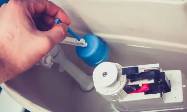 Main d'homme ajustant le flotteur bleu d'une chasse d'eau qui ne se remplit pas pour un wc suspendu.