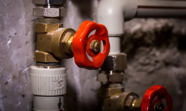 Gros plan sur un joint d'électrovanne avec une poignée rouge vif, faisant partie d'un système de plomberie complexe.