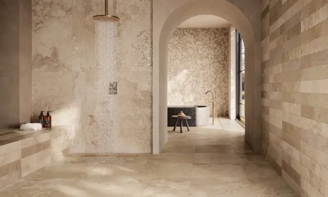 Douche moderne avec robinetterie dorée sur un sol de salle de bain en travertin. L'espace invite à la détente.