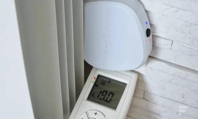 Schéma branchement thermostat chauffage électrique : un boîtier blanc "heatzy" et une télécommande affichant 19.0°C, près d'un radiateur.