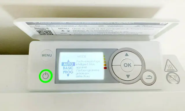 Thermostat sur radiateur électrique. L'écran affiche "MODE AUTO" pour un pilotage intelligent. Le bouton d'alimentation est allumé en vert.