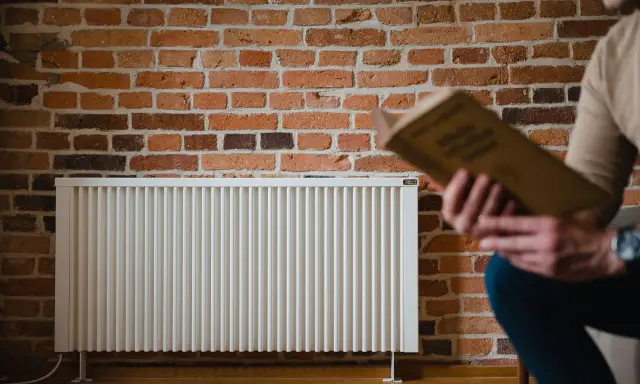 Un homme lit un livre près d'un radiateur blanc. La question quelle puissance de radiateur pour 25 m2 est au cœur de ce décor cosy.