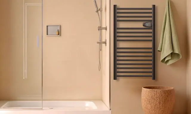 Salle de bain moderne avec douche, porte-serviettes chauffant noir et panier en liège. Le disjoncteur du sèche serviette est visible.