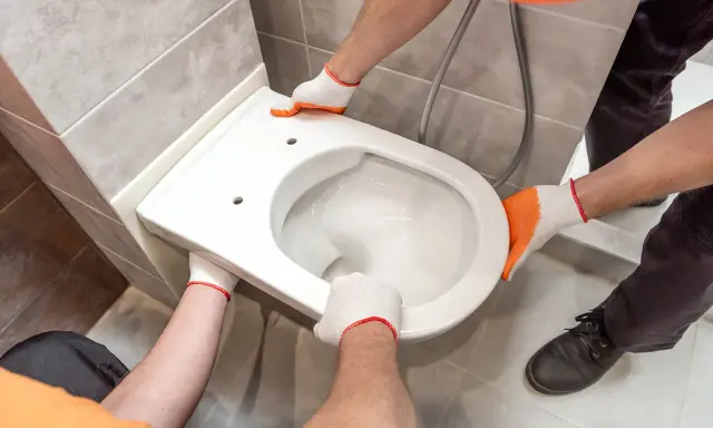Mains gantées installent un WC suspendu. L'opération est délicate, mais le résultat sera moderne et pratique.