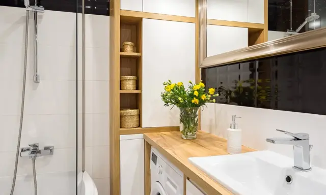 Une petite salle de bain moderne avec une douche, un lavabo, une machine à laver et des paniers en osier sur des étagères en bois.