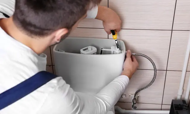 Un plombier répare une chasse d'eau qui coule. Il utilise une pince pour ajuster le mécanisme interne du réservoir.