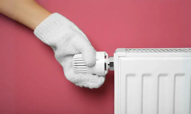 Main tenant, avec un gant blanc, ajuste le thermostat d'un radiateur pour choisir entre le chauffage mode eco ou confort.