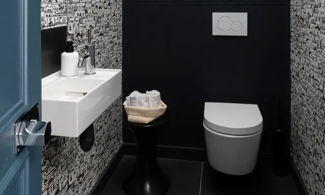 Une salle de bain moderne avec un papier peint original, un petit lavabo blanc, des serviettes roulées et une cuvette suspendue. La deco wc est soignée.