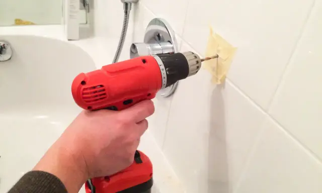 Main tenant perce le carrelage de la salle de bain pour installer un accessoire.