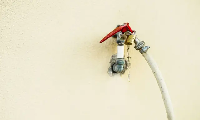 Robinet extérieur avec un cadenas doré et un tuyau blanc, le raccord asymétrique suggère une utilisation inhabituelle.