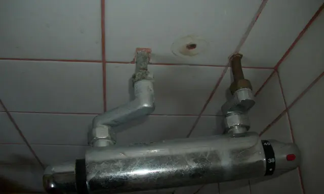 Un excentrique robinet de douche, fixé au mur carrelé, avec des tuyaux argentés et des indications de température.