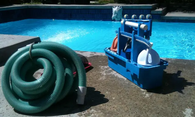 Tuyau vert enroulé et boîte bleue d'accessoires de nettoyage pour le branchement piscine.