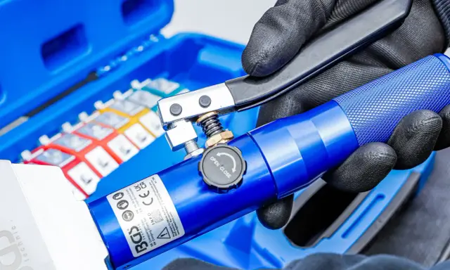 Main bleue avec un outil de sertissage. Le kit contient des cosses colorées.
