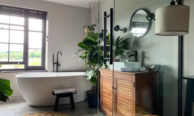 Une salle de bain moderne et épurée, parfaite pour refaire salle de bain. Baignoire îlot, meuble en bois, plantes vertes et lumière naturelle.