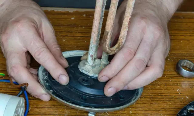 Mains de l'homme ajustant un élément chauffant entartré sur un joint plat, prêt pour le remplacement.