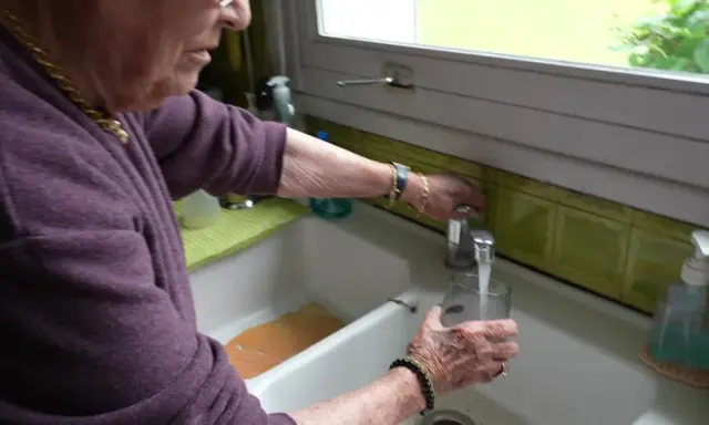 Une femme remplit un verre d'eau du robinet. L'eau de Beauvais coule fraîchement.