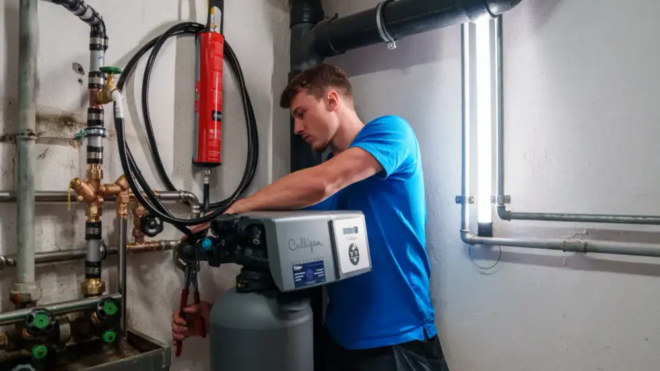 Un technicien installe un adoucisseur d'eau Culligan. Il utilise une pince pour ajuster les tuyaux en cuivre.
